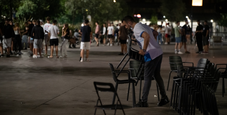 Un cambrer recull una terrassa mentre diverses persones es concentren al Passeig | Roger Benet