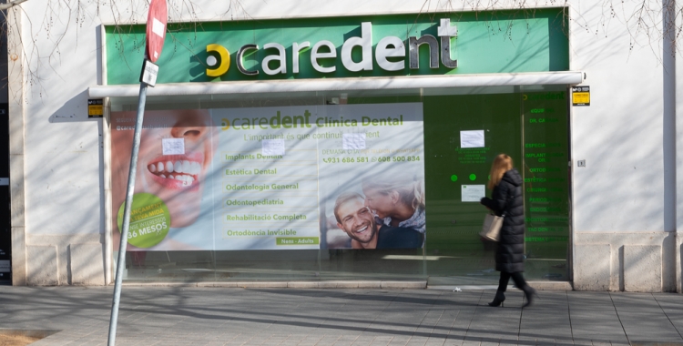 Una dona es mira els cartells als vidres de la clínica Caredent del Passeig | Roger Benet