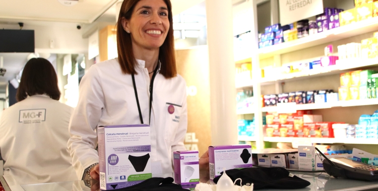 Una farmacèutica darrere del mostrador amb diversos productes menstruals com ara les calces