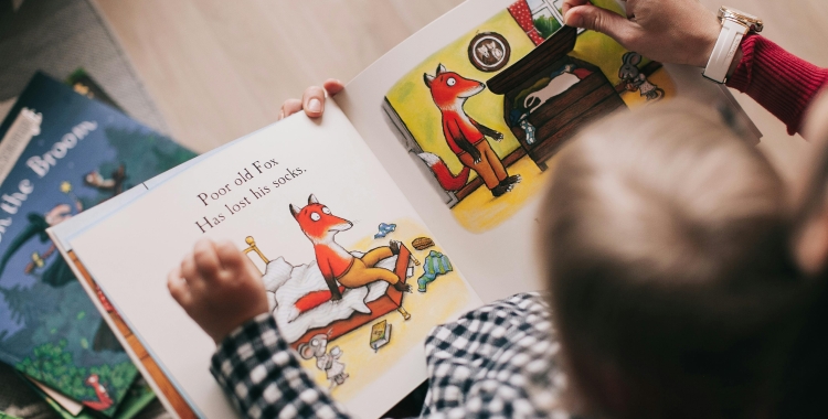 Una criatura llegint acompanyada de la seva família | Pexels