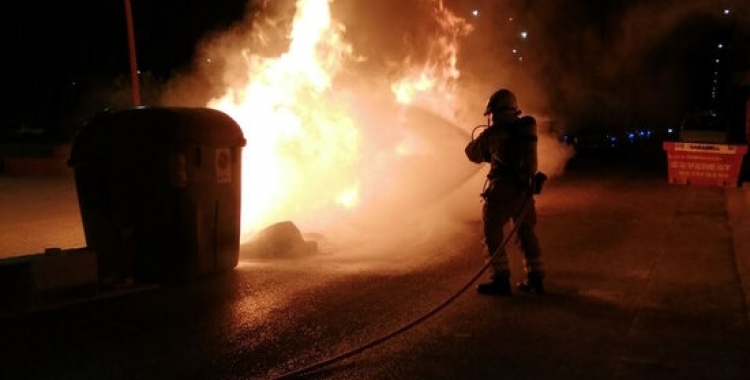 Un bomber apagant l'incendi en un contenidor